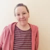 Picture of lady with hair tied back in striped top and pink jacket